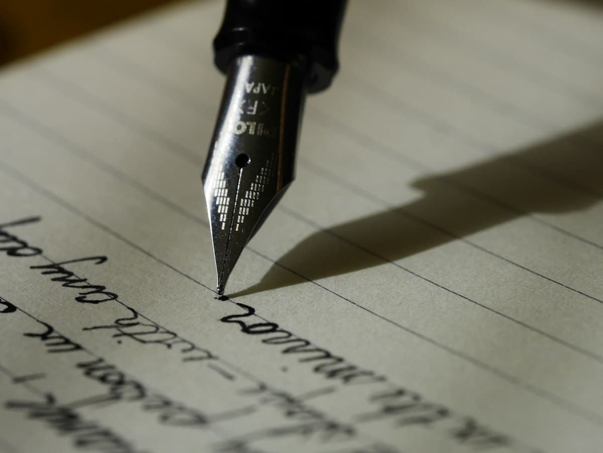 Classic fountain pen resting on open lined notebook with handwritten essay draft