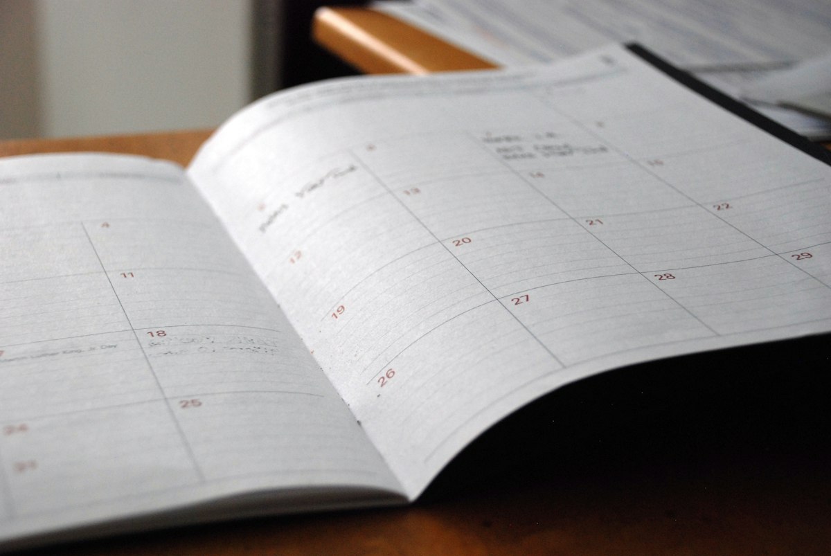 Workspace with daily planner notebook, coffee mug, and glasses marking milestones